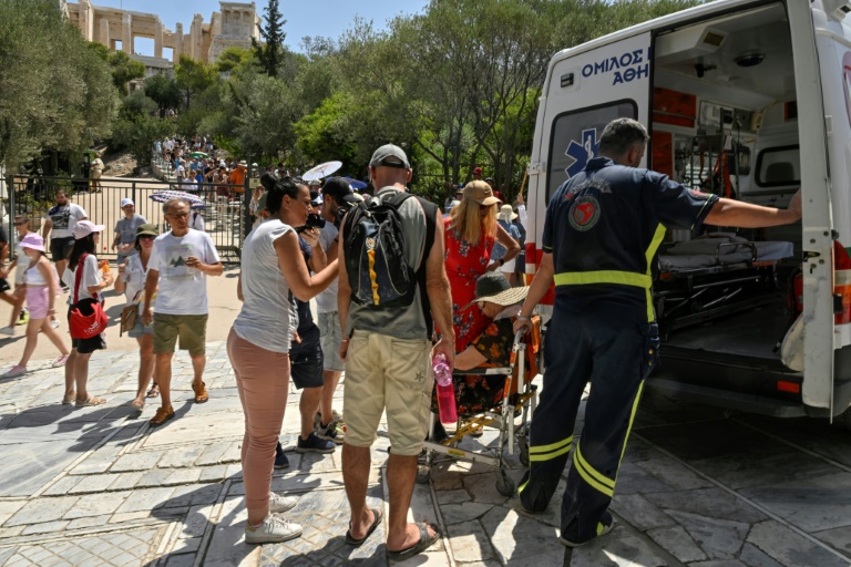 Ένας ηλικιωμένος τουρίστας περιθάλπεται από έναν οδηγό ασθενοφόρου μετά από λιποθυμία κατά τη διάρκεια επίσκεψης στην Ακρόπολη στις 20 Ιουλίου 2023 στην Αθήνα (AFP - Λουίζα Γκουλιεμάκη)
