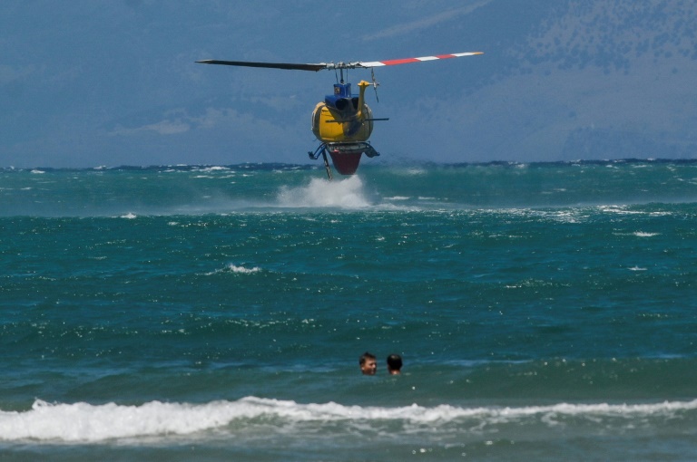 Ένα πυροσβεστικό ελικόπτερο γεμίζει με νερό κοντά σε λουόμενους στις 27 Ιουλίου 2023 στο νησί της Κέρκυρας, Ελλάδα (AFP - Armend NIMANI)